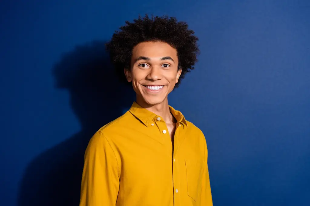 Eine Person mit gelbem Oberteil lächelt in die Kamera